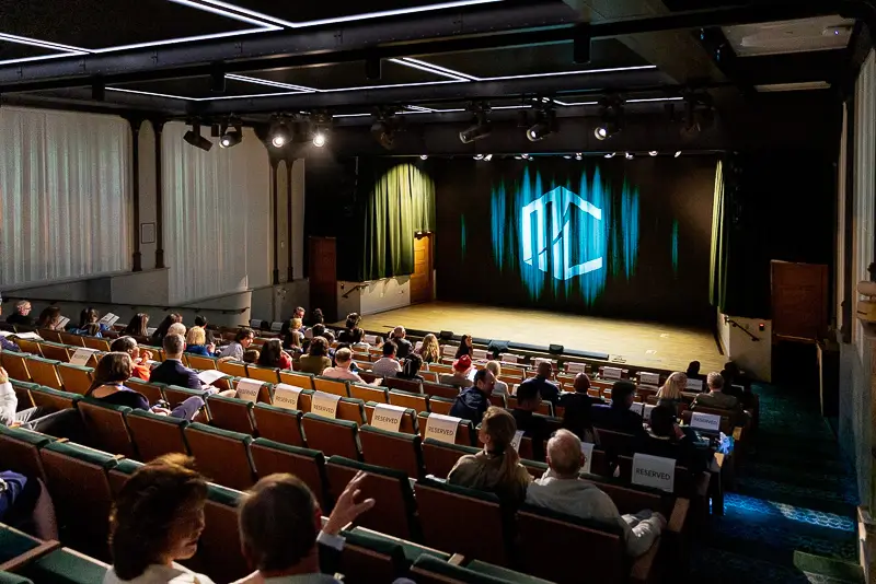 Wide view of a Washington DC fundraising gala with a large stage, dramatic lighting, and a full seated audience