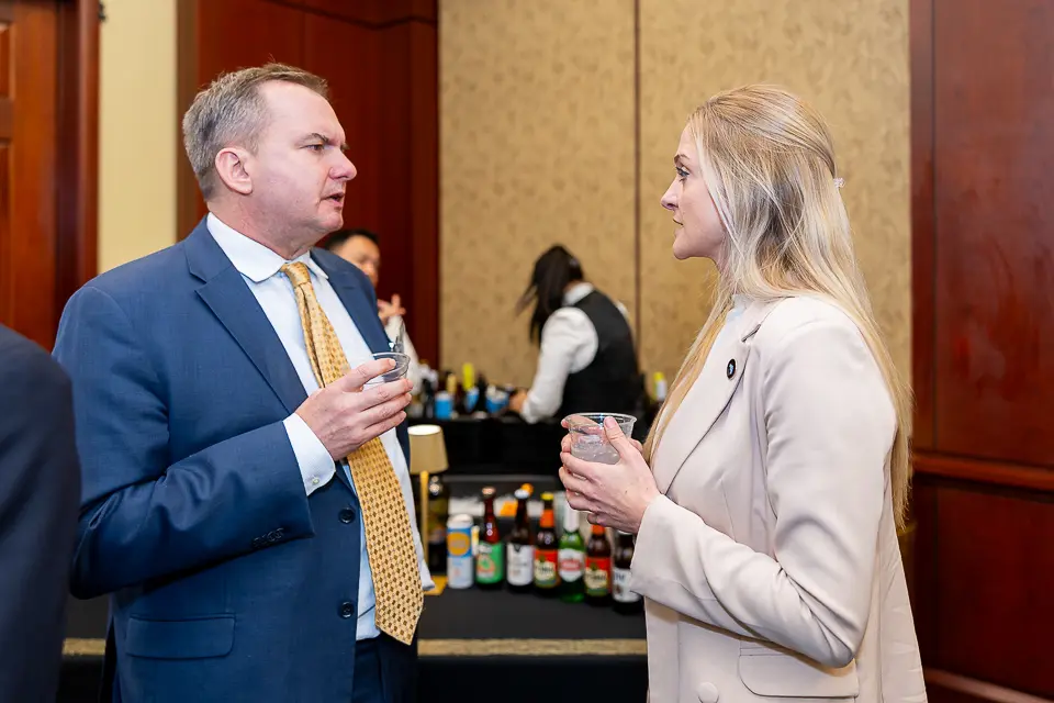 Two corporate event guests speaking during a Washington DC reception with a bar setup in the background