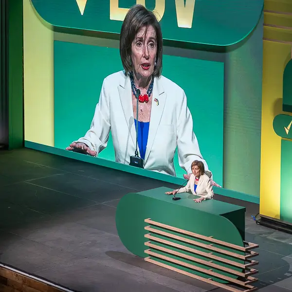 Speaker delivering remarks at a conference stage in Washington DC with large projection screen during a corporate or government event