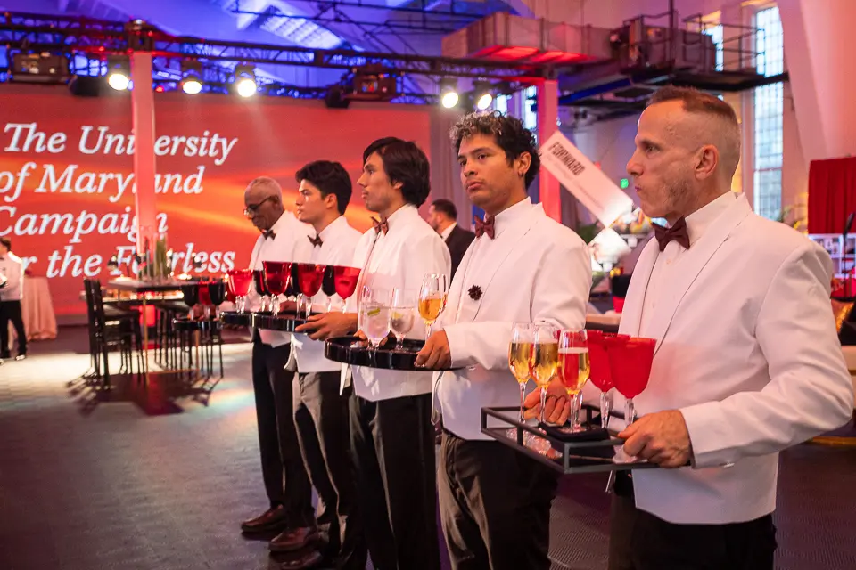 Catering team serving red drinks beneath University of Maryland Forward campaign graphics