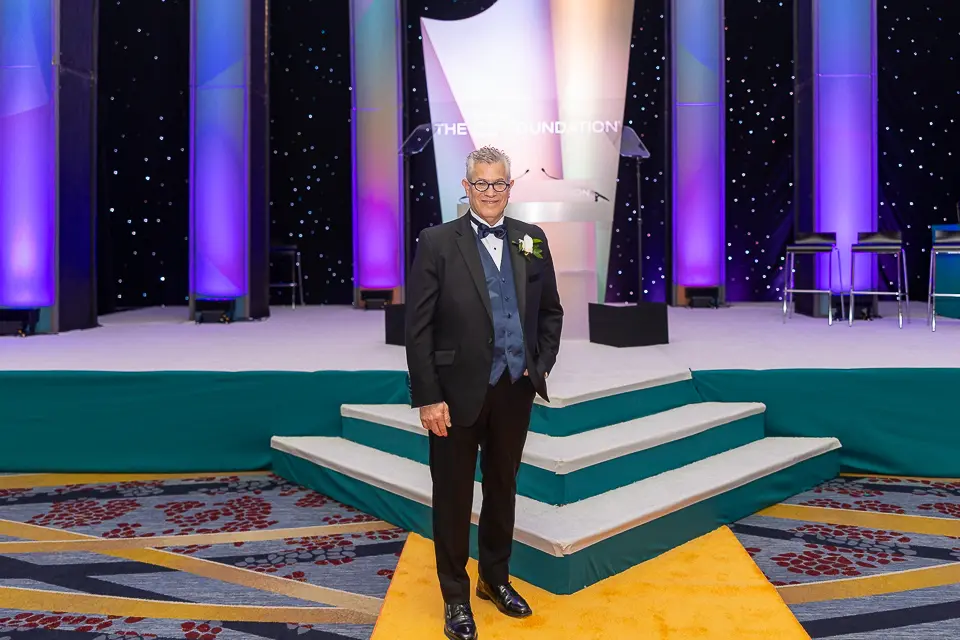 Formal guest portrait on the Herb Wegner Awards 2026 stage with purple lighting and a green carpet.